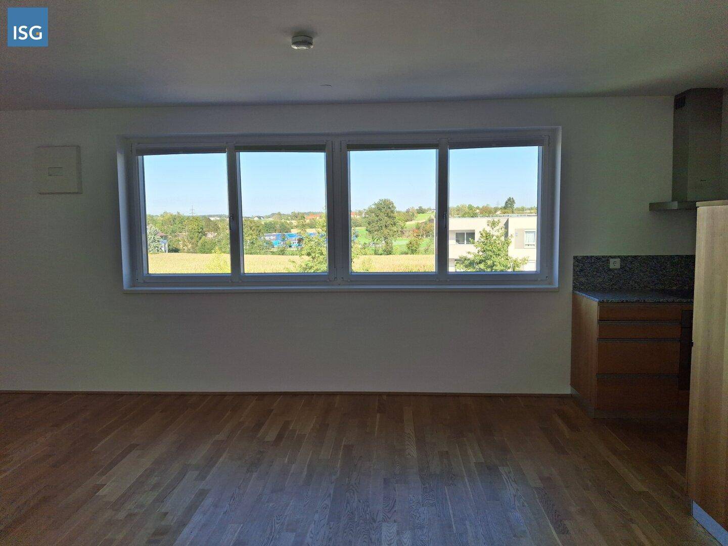 Heller Wohnbereich mit Parkettboden und großen Fenstern, die einen weiten Ausblick bieten.