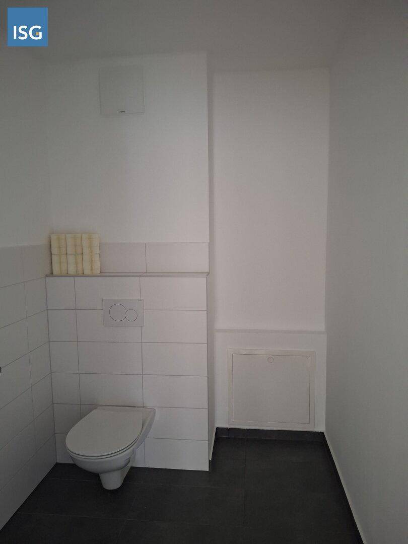 Einfaches Gäste-WC mit weiß gefliesten Wänden und dunklem Boden, funktional gestaltet.