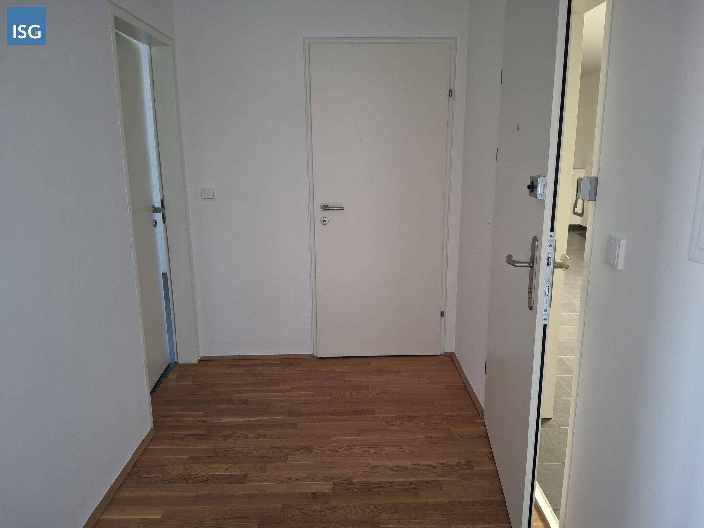 Geräumiger Flur mit Parkettboden und mehreren Türen, inklusive der Eingangstür.