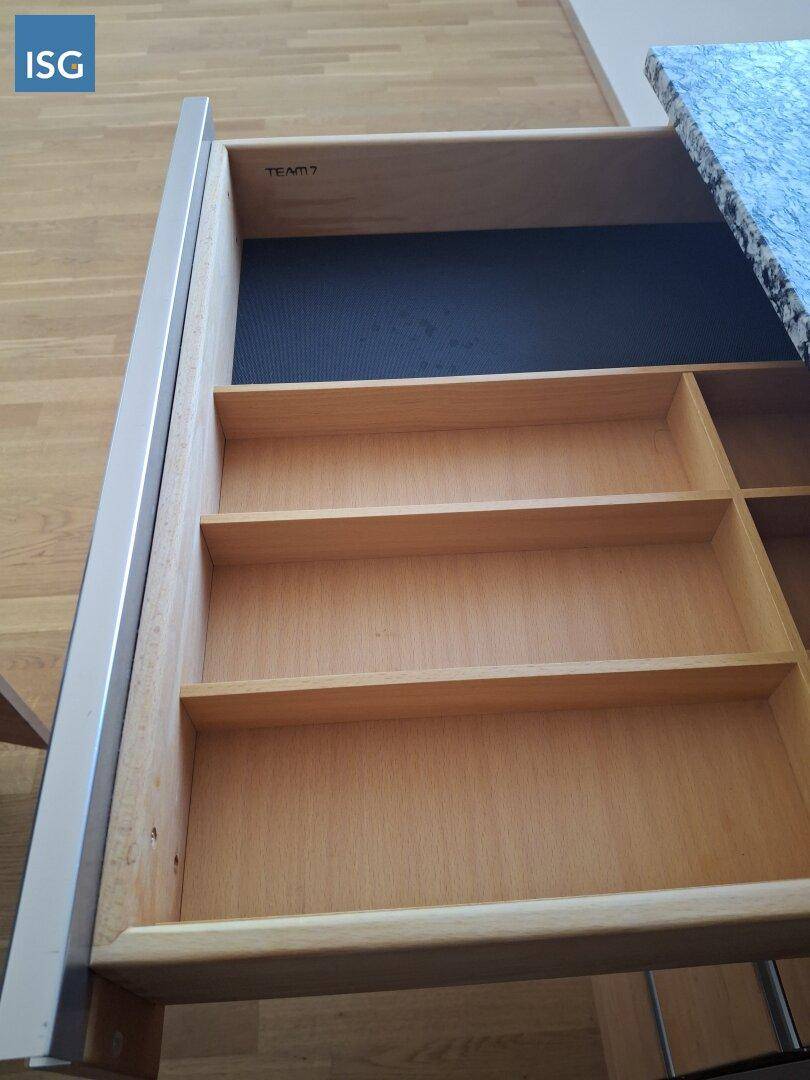 Ausgezogene Schublade einer Holzküche mit Besteckorganisation und "TEAM 7" Branding.