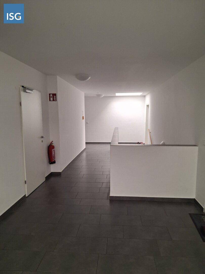 Langer, heller Flur mit dunklen Fliesen und einem Feuerlöscher an der Wand.