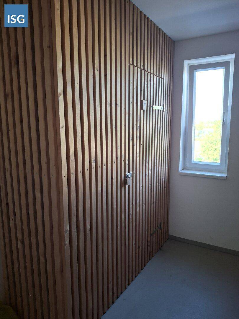 Raum mit vertikaler Holzverkleidung an der Wand und einem Fenster, möglicherweise ein Abstellraum.