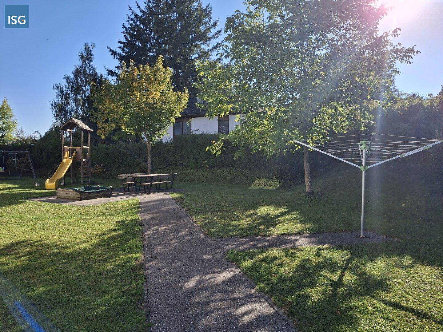 Gemeinschaftlicher Gartenbereich mit Spielplatz, Rutsche und Wäschespinne unter Bäumen.