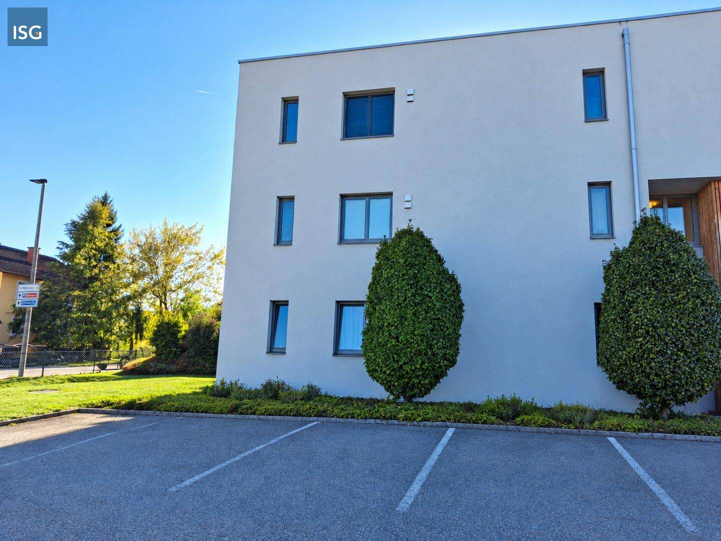 Ansicht eines modernen Gebäudes mit weißer Putzfassade, umgeben von Bäumen und einem Außenparkplatz.
