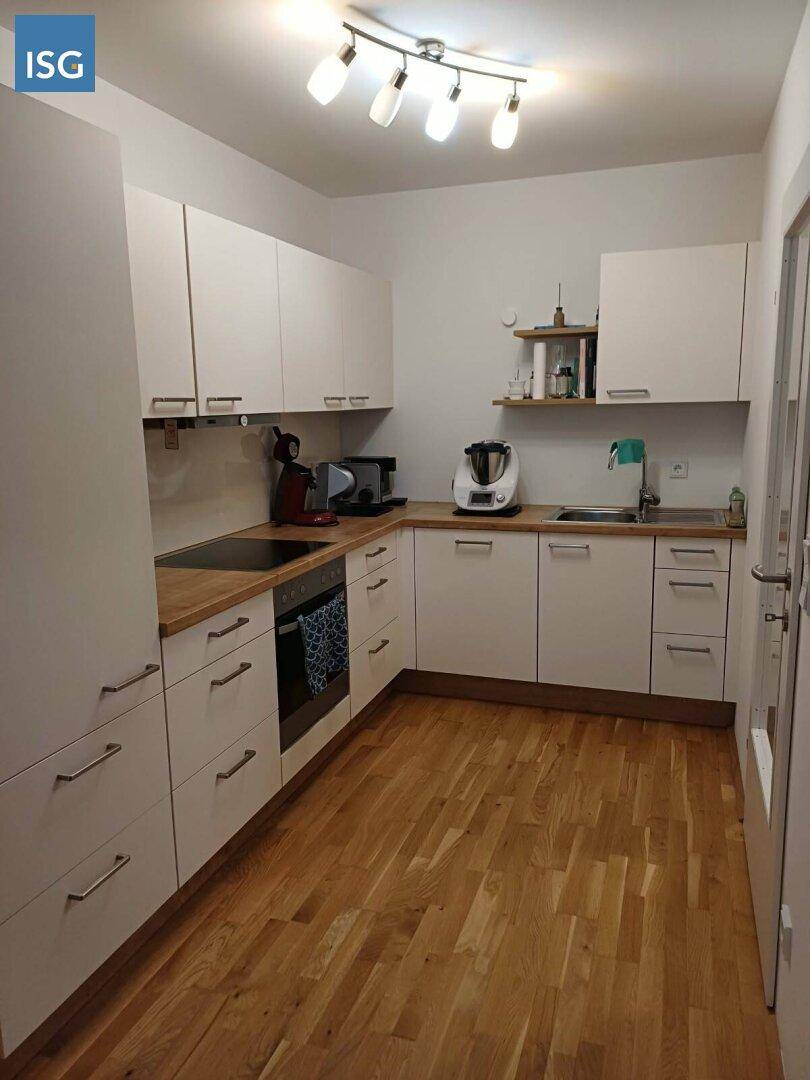 Helle Einbauküche mit weißen Schränken, Holz-Arbeitsplatte und Parkettboden.
