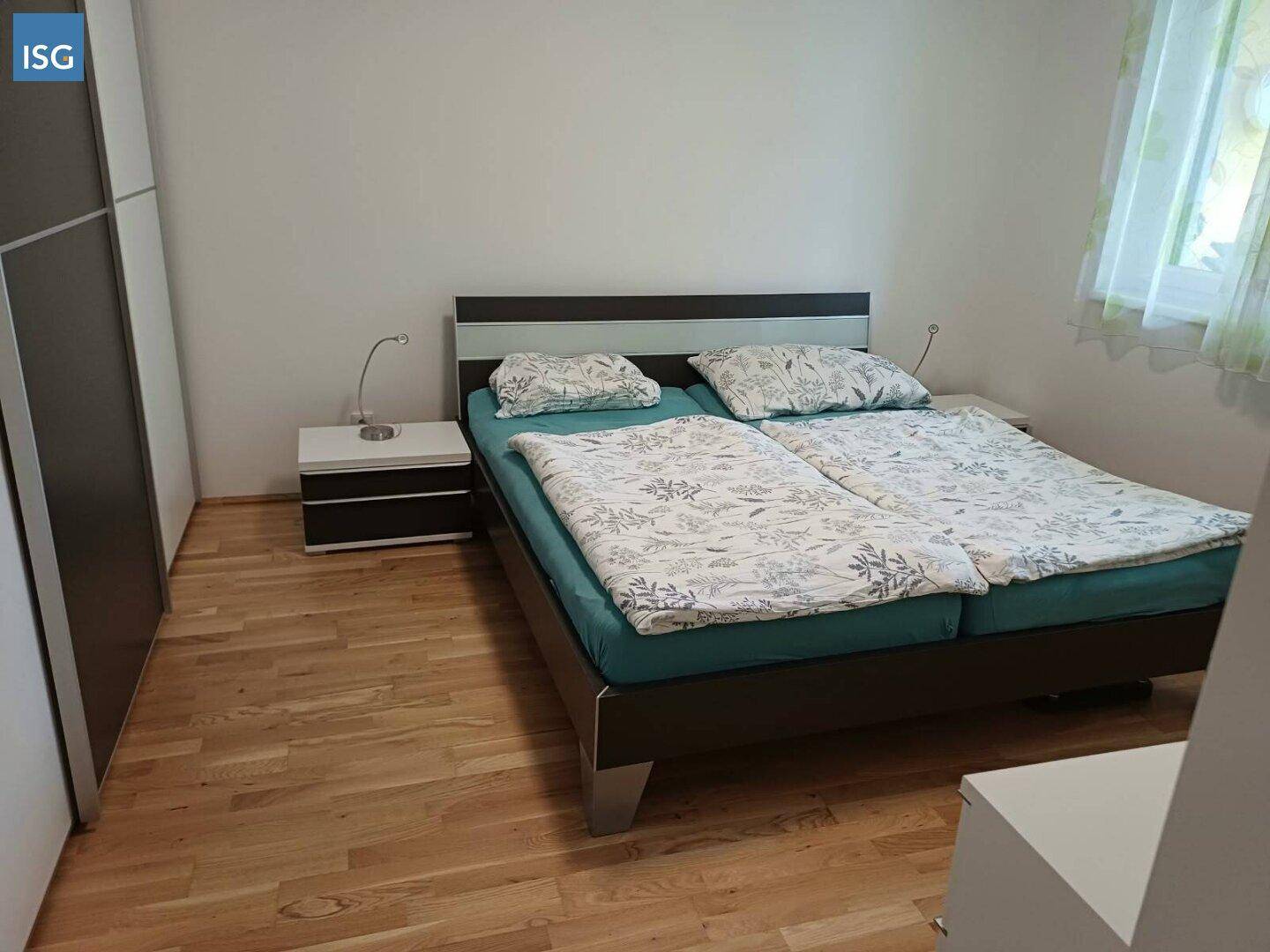 Schlafzimmer mit Doppelbett, Nachttischen und hellem Holzparkettboden.
