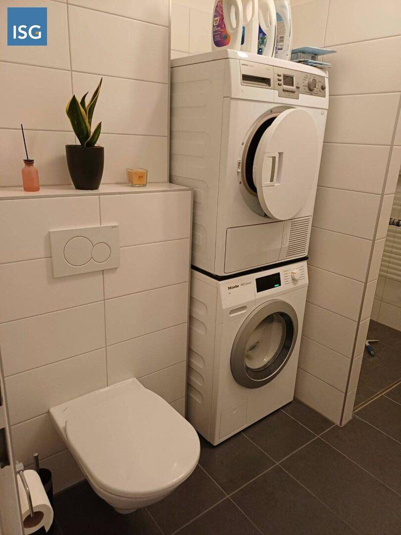 Modernes WC mit Wand-WC, Waschmaschine und Trockner in platzsparender Stapelanordnung.