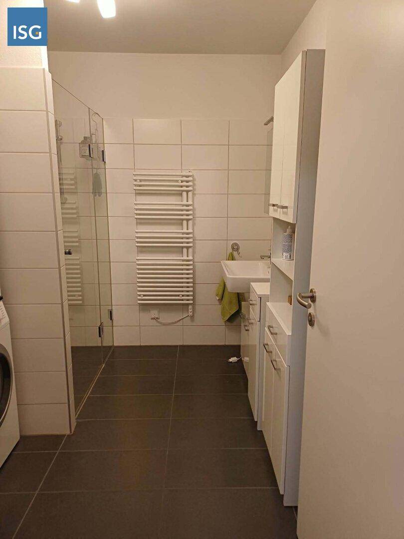 Helles Badezimmer mit ebenerdiger Dusche, Waschbecken und beheiztem Handtuchhalter.