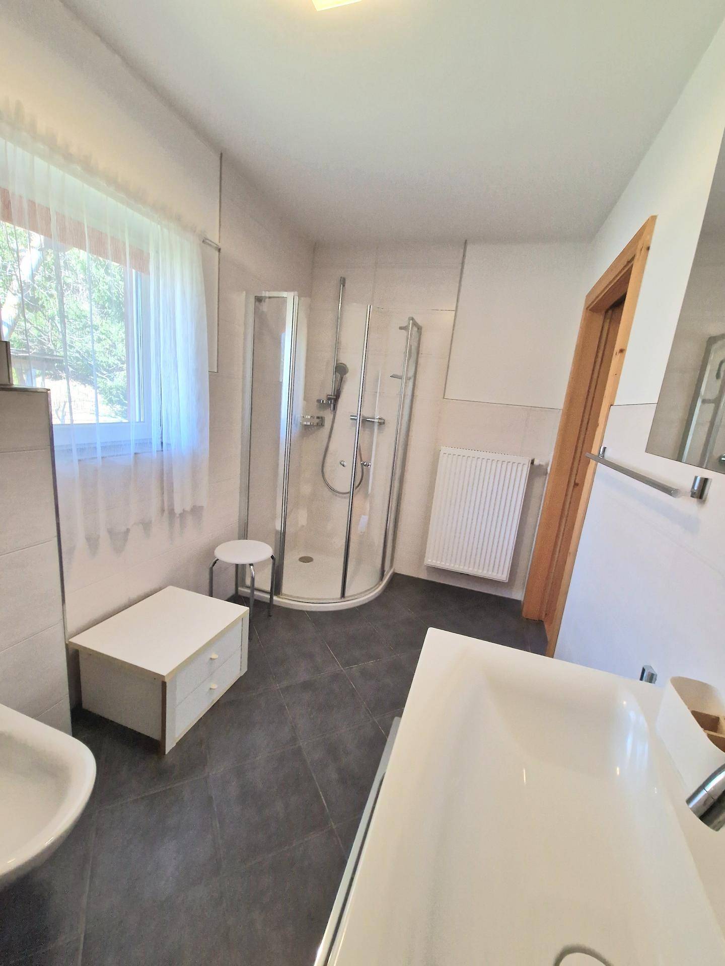 Modernes Badezimmer mit dunklen Fliesen, Duschkabine und einem Fenster für Tageslicht.