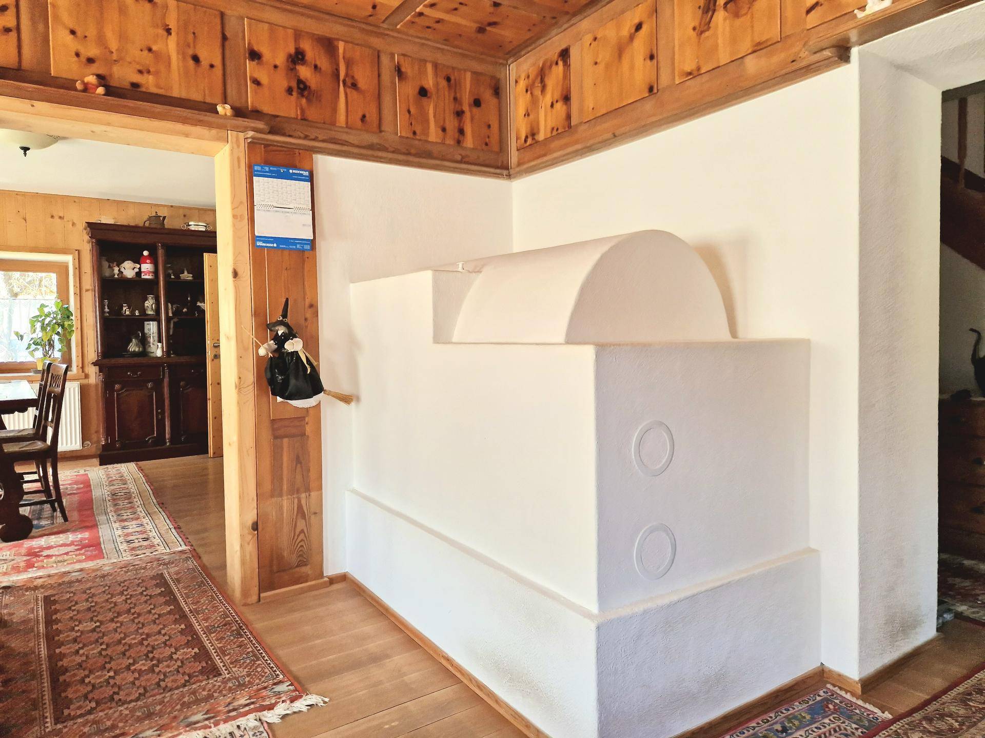 Traditioneller Kachelofen in einem Raum mit Holzboden und Zugang zu einem Essbereich.
