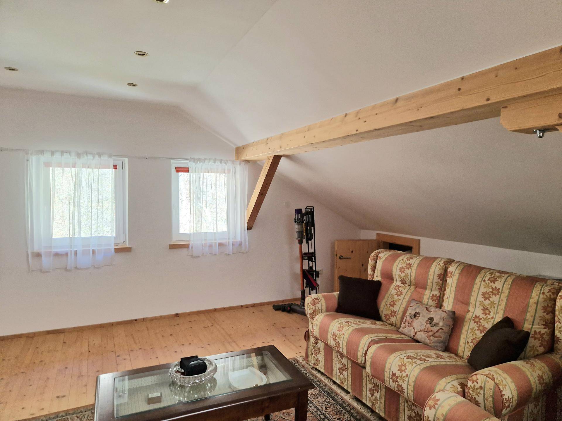 Gemütliches Wohnzimmer im Dachgeschoss mit schrägen Wänden, Holzbalken und einem Sofa.