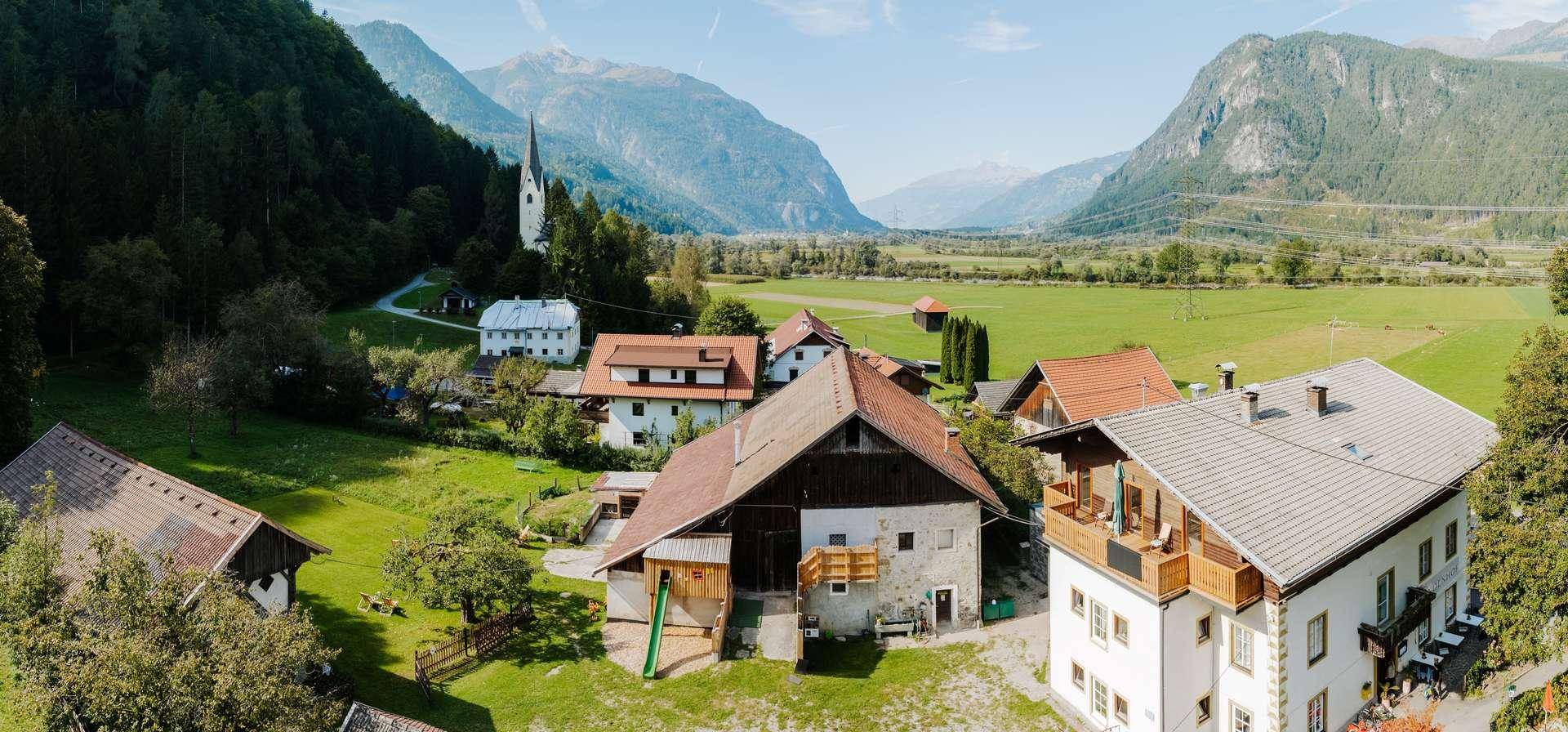 Malerische Luftaufnahme eines Dorfes in einem Tal mit Bergen, grünen Wiesen und traditionellen Häusern.