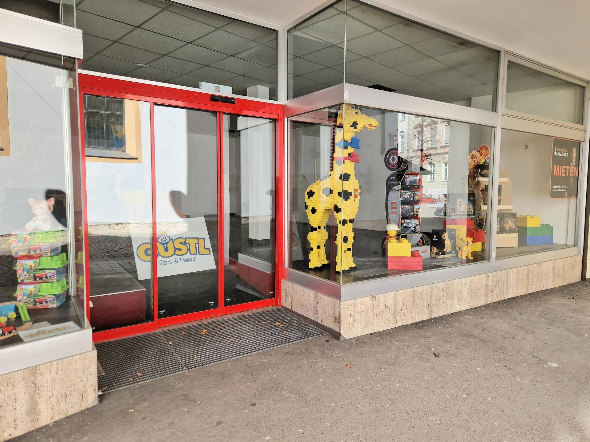 Eingangsbereich eines Geschäfts mit automatischen Glastüren und Schaufenstern, die bunte Spielzeuge ausstellen.