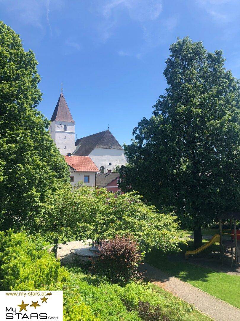 Historische Kirche mit hohem Turm, umgeben von üppigen grünen Bäumen und einem Spielplatz.