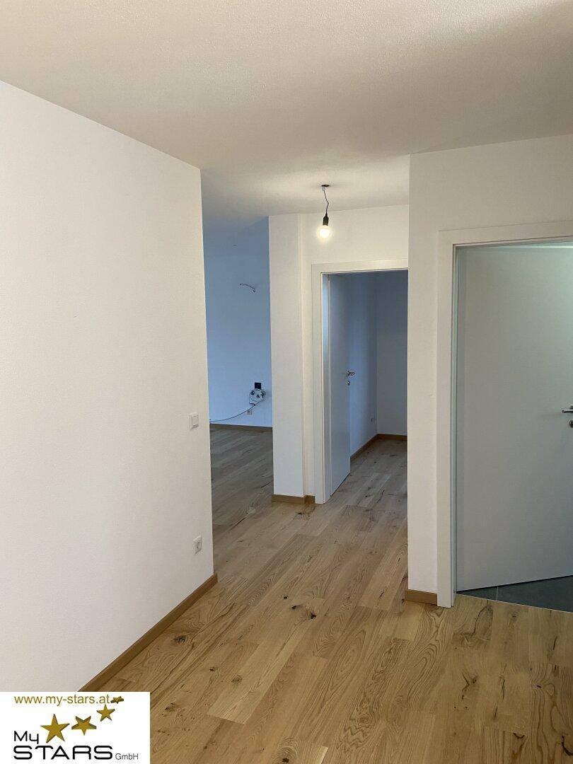 Heller Flur mit hochwertigem Holzboden und weißen Wänden, der zu weiteren Räumen führt.