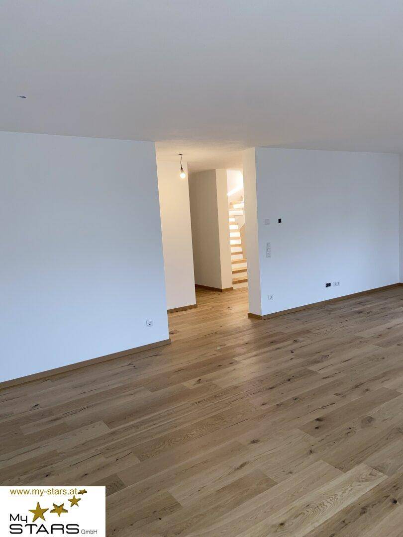 Offener Wohnbereich mit elegantem Holzboden und Zugang zu einer modernen Treppe.