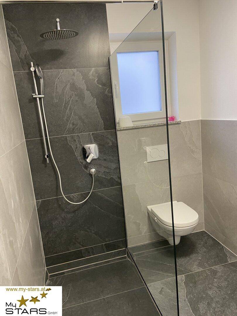Zeitgemäßes Badezimmer mit ebenerdiger Dusche, Wand-WC und eleganten grauen Fliesen.