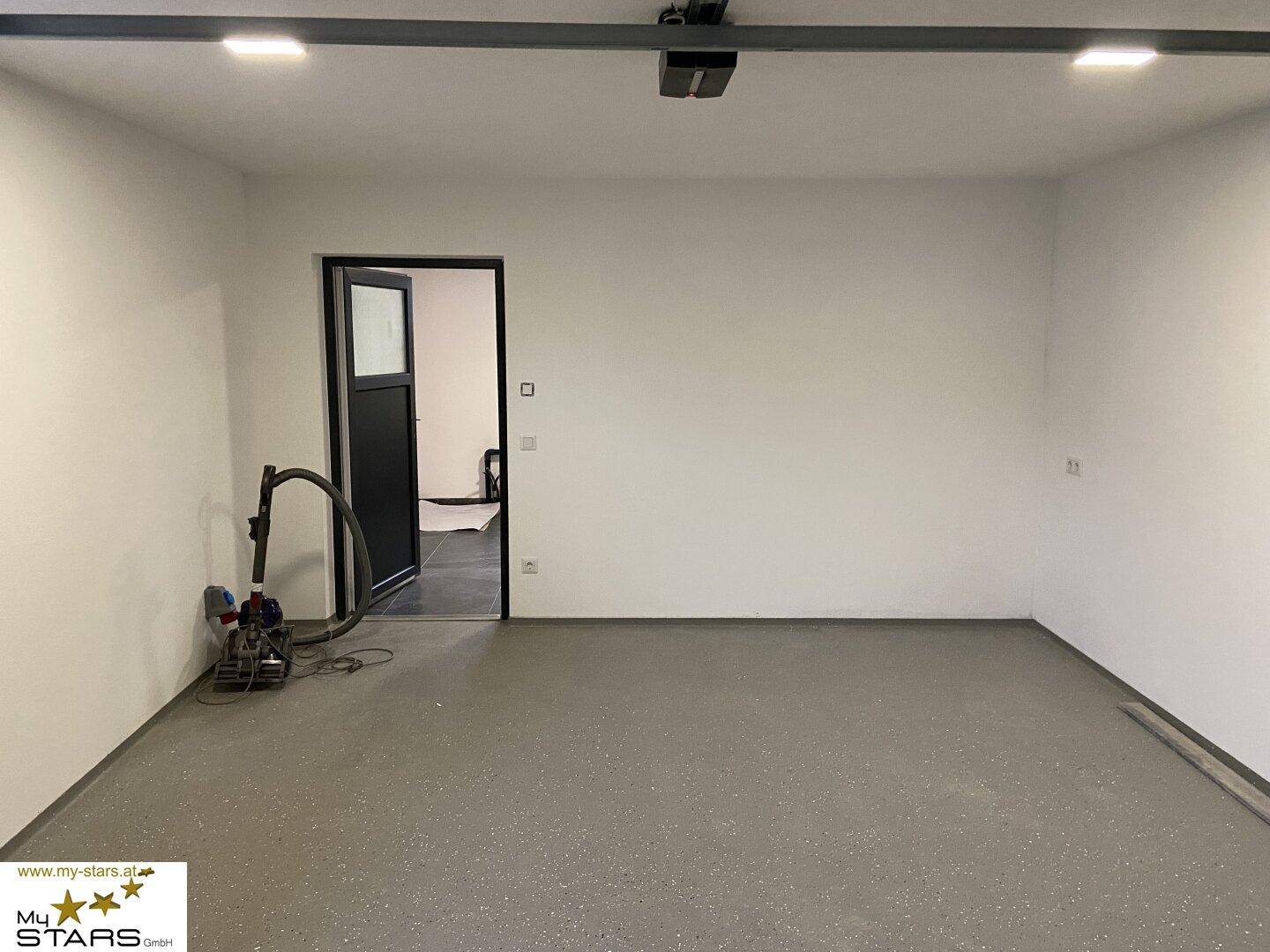 Geräumige Garage oder Abstellraum mit robustem Betonboden und weißen Wänden.