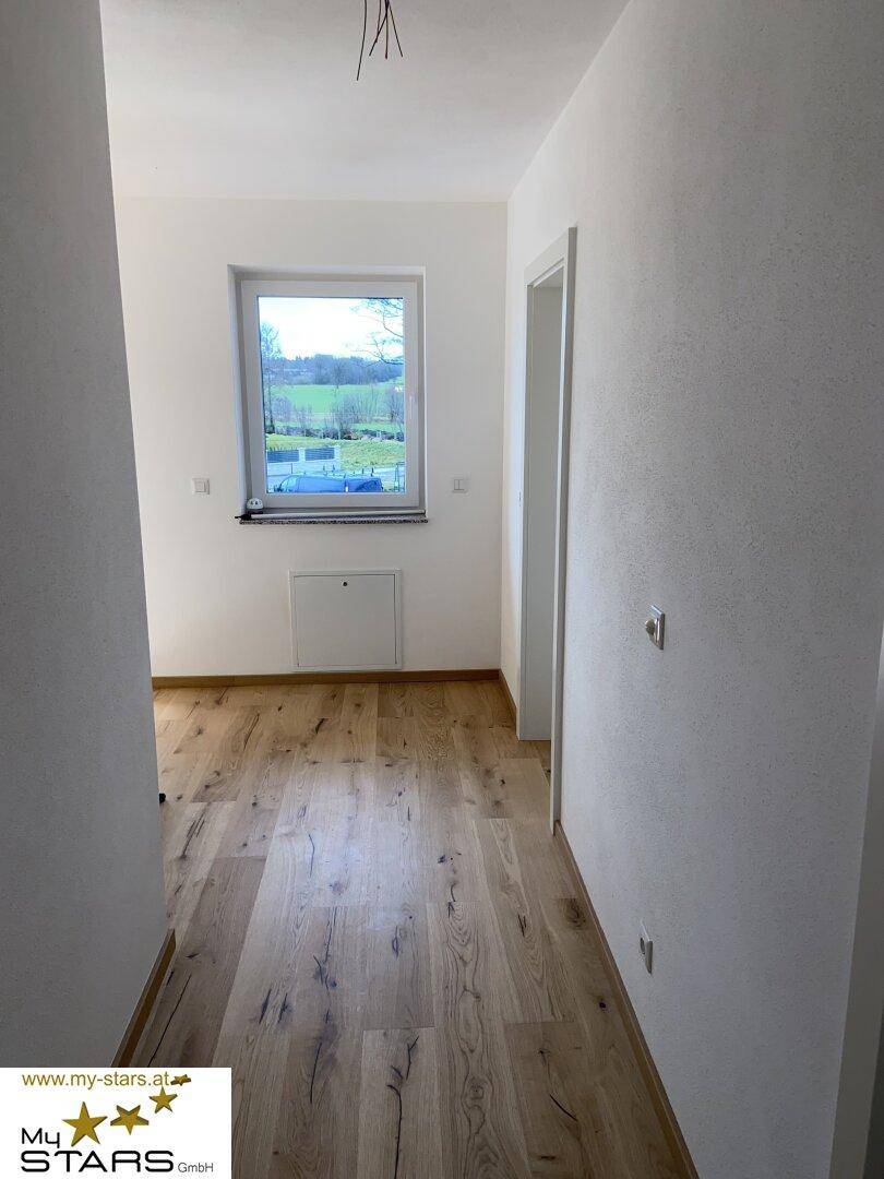 Heller Raum mit Holzboden und einem Fenster, das einen schönen Blick ins Grüne bietet.