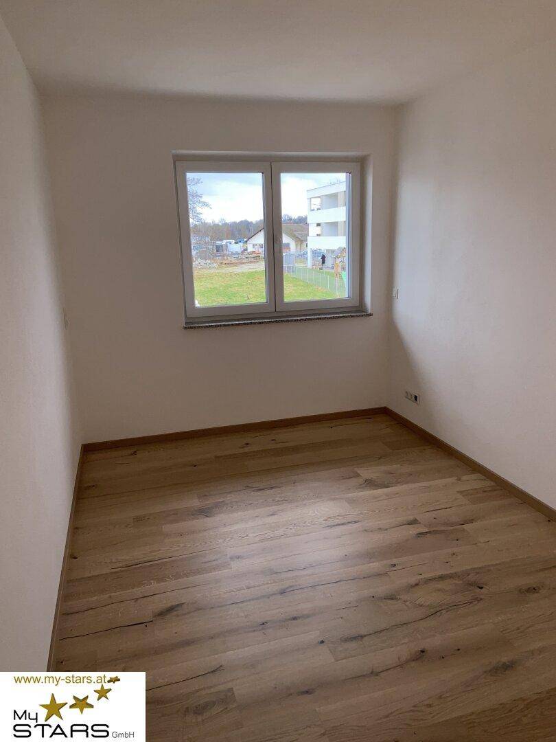 Helles Schlafzimmer mit Holzboden und einem Fenster, das viel Tageslicht hereinlässt.