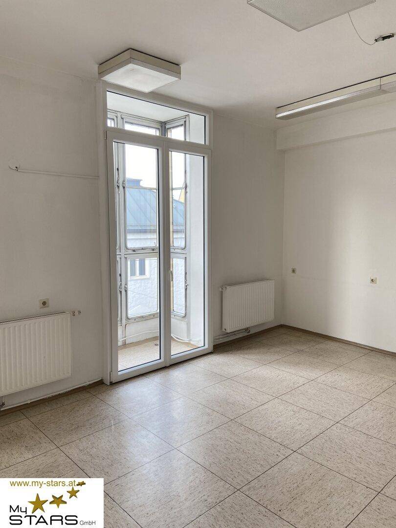 Geräumiger Büroraum mit großen Fenstern, die viel Tageslicht hereinlassen, und neutralen Fliesen.