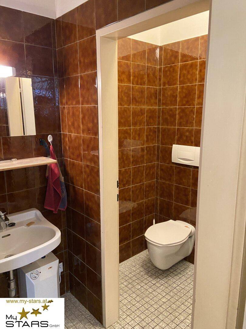 Kleines Badezimmer mit braunen Fliesen an den Wänden, einem Waschbecken und einer Toilette.