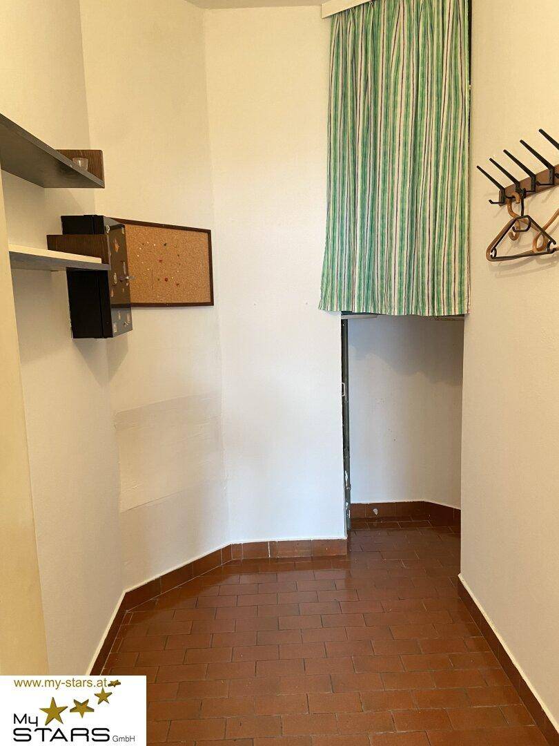 Eingangsbereich mit Terrakotta-Fliesenboden, weißen Wänden und einer Garderobe.