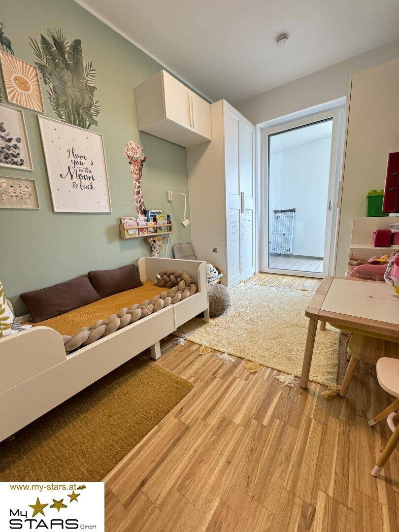 Kinderzimmer mit Holzboden, hellem Bett und verspielter Wanddekoration.