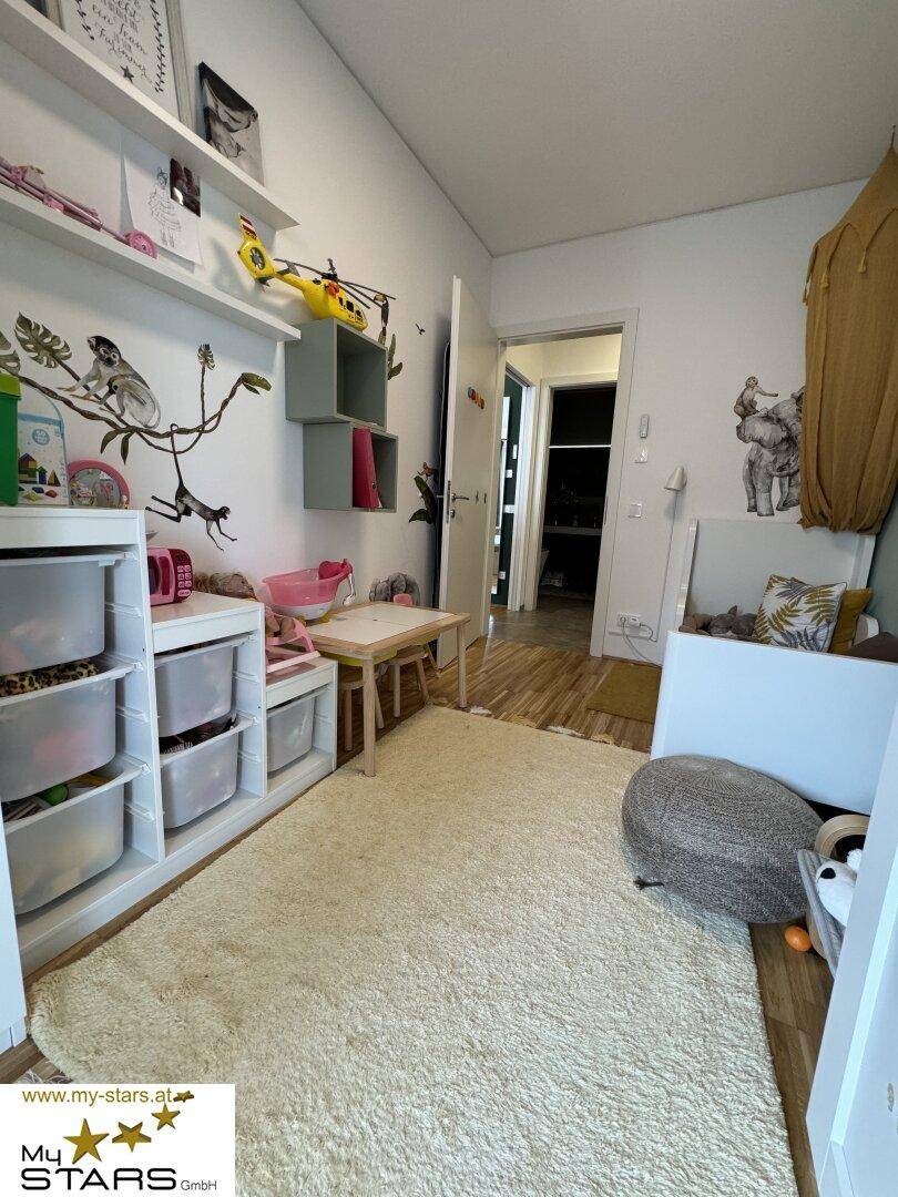Helles Kinderzimmer mit Teppichboden, Spielzeug und Stauraum.