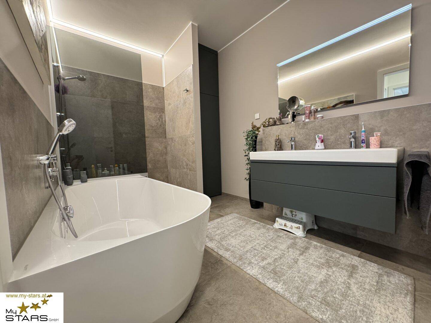 Modernes Badezimmer mit freistehender Badewanne, Doppelwaschbecken und großem Spiegel.