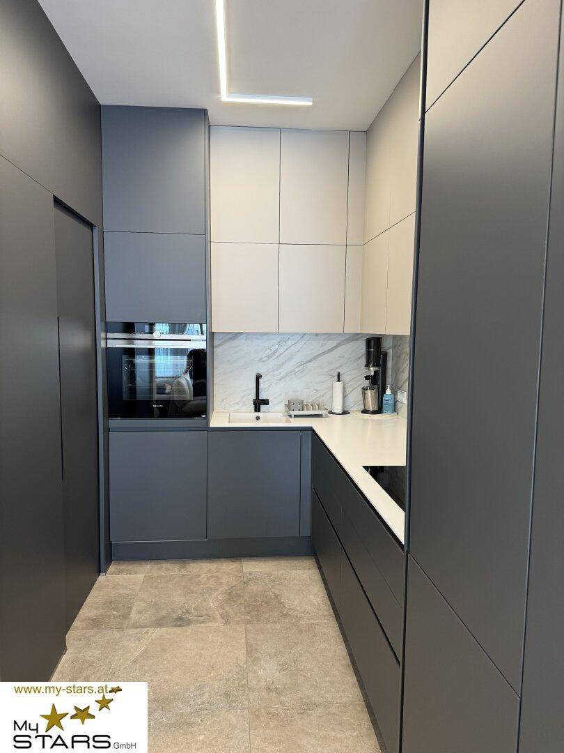 Moderne Küche mit grauen und weißen Schränken, integrierten Geräten und Marmor-Rückwand.