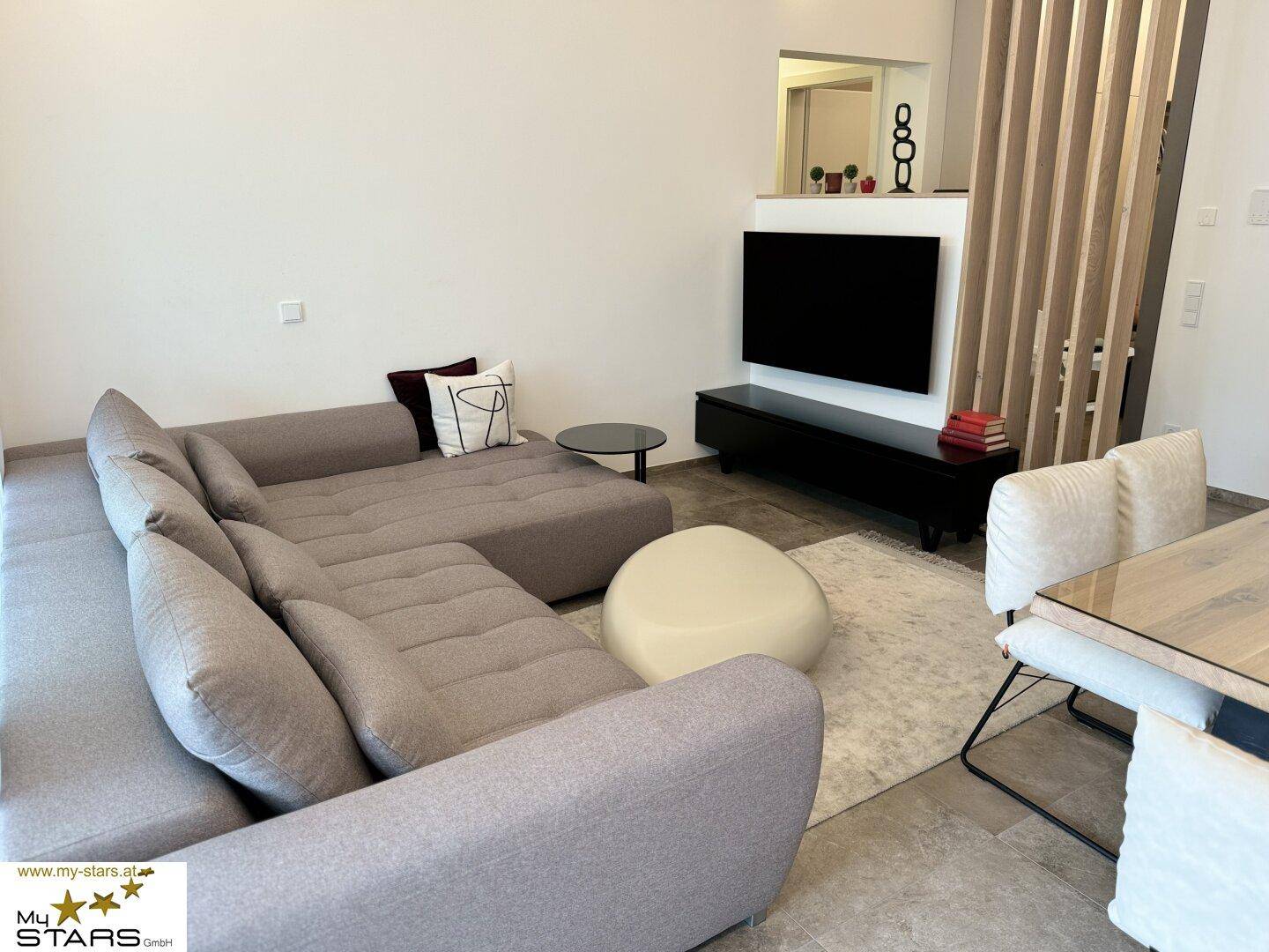 Gemütliches Wohnzimmer mit großem Ecksofa, Fernseher und modernem Teppich.
