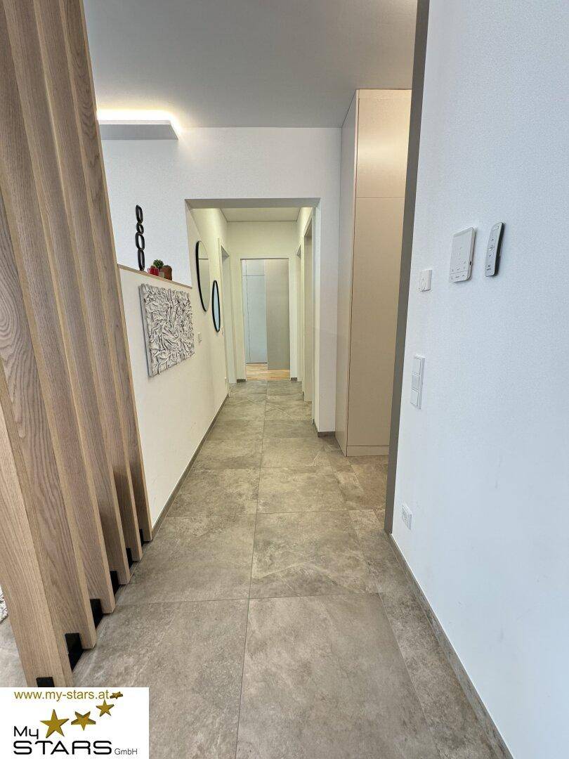 Moderner Flur mit Fliesenboden, Holzlamellenwand und indirekter Beleuchtung.