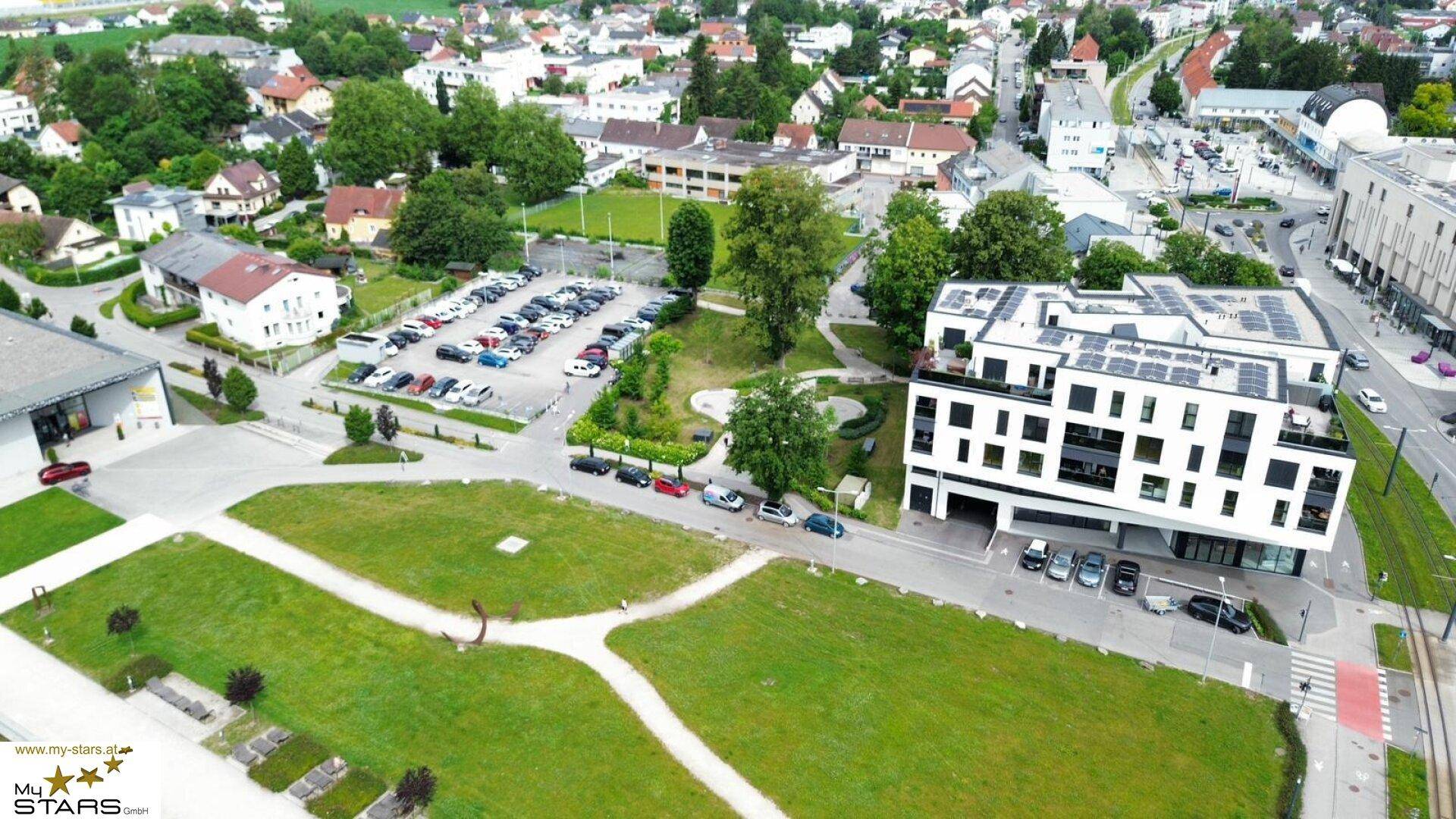 Luftaufnahme eines modernen Gebäudes mit Solarpaneelen und weitläufigen Grünflächen.