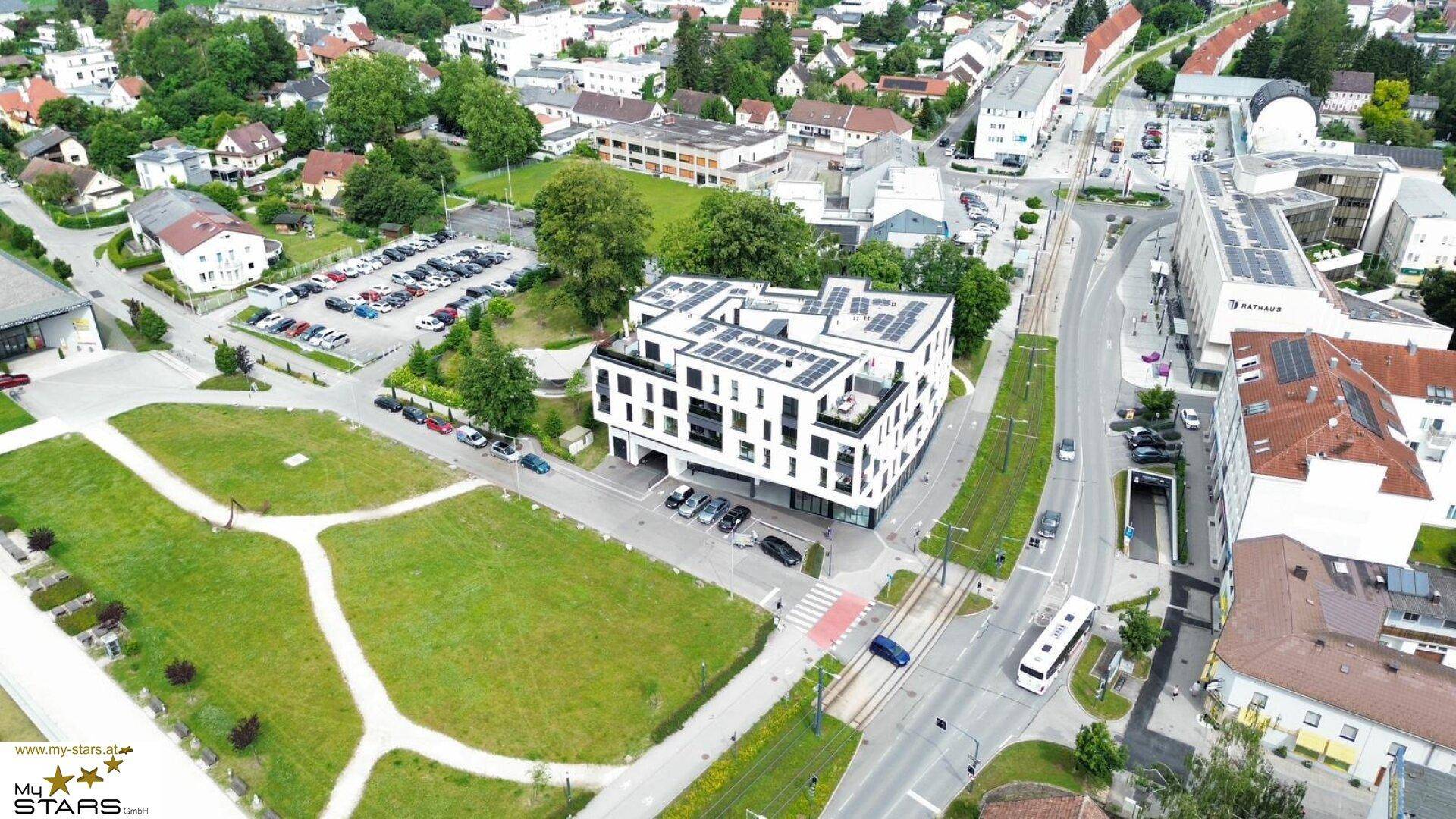 Moderne Wohnanlage mit Photovoltaikanlage auf dem Dach, umgeben von Grünflächen und städtischer Infrastruktur.