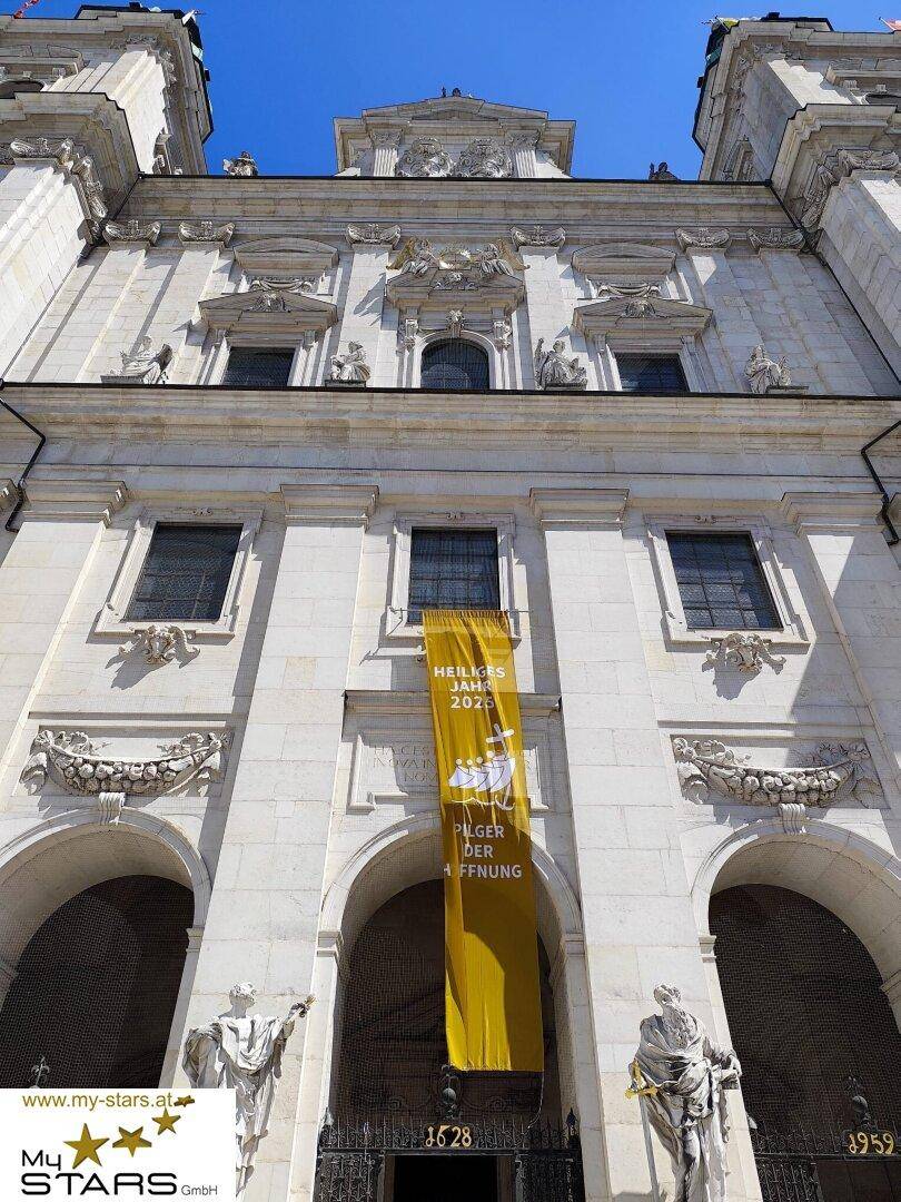 Detailansicht der barocken Fassade des Salzburger Doms mit Skulpturen und einem Banner.