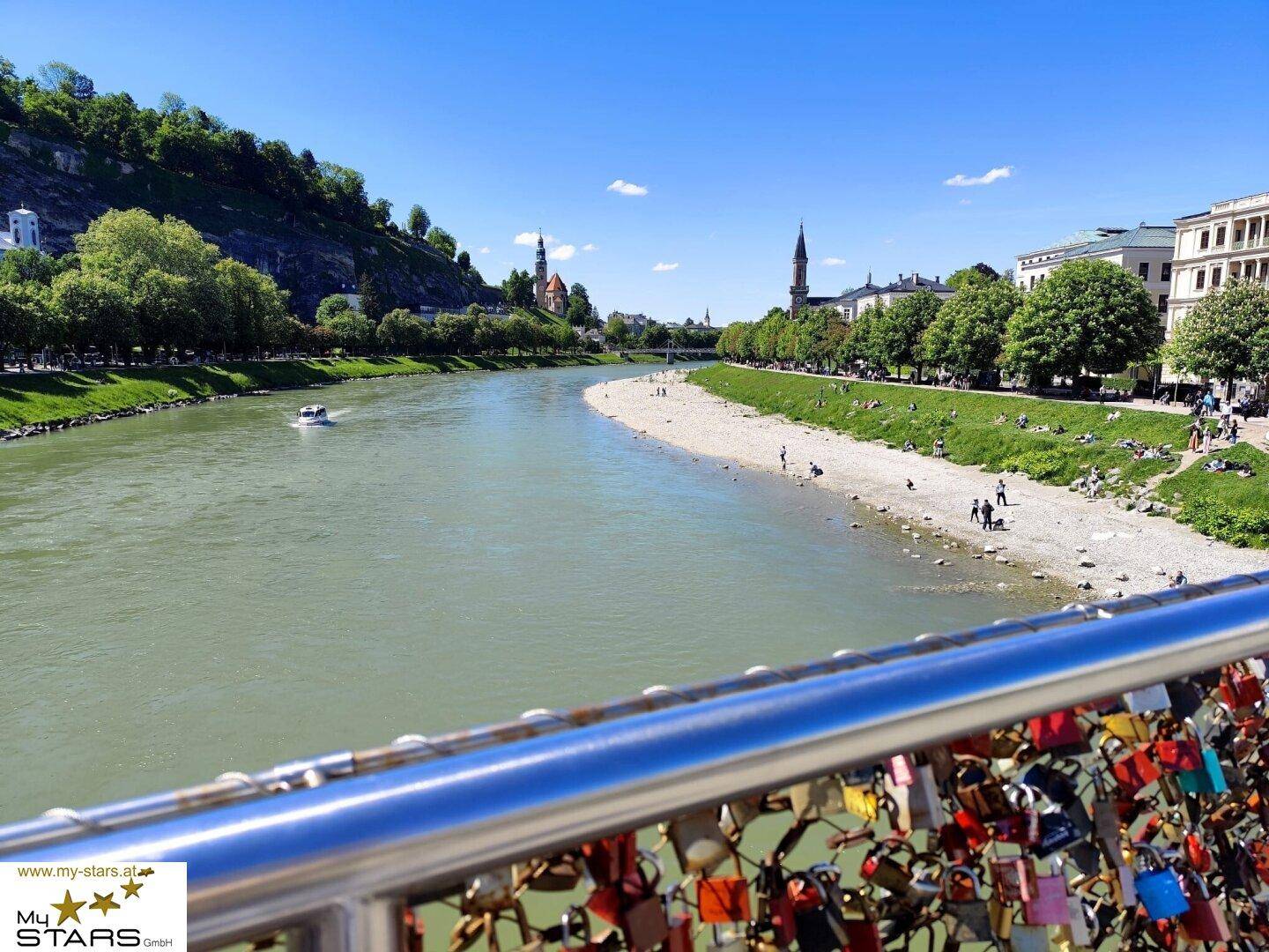 Malerischer Blick auf die Salzach mit der Altstadt und grünen Ufern im Sonnenschein.