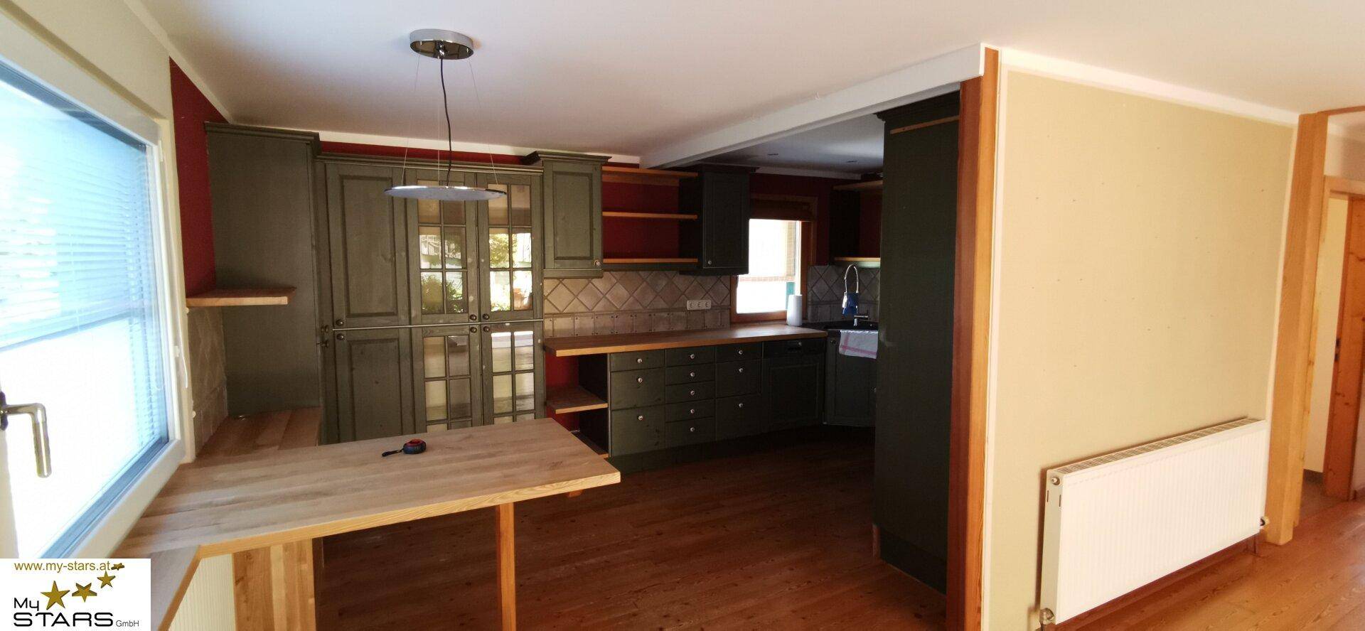Rustikale Küche mit dunklen Holzschränken, Holzboden und einem kleinen Frühstückstresen am Fenster.