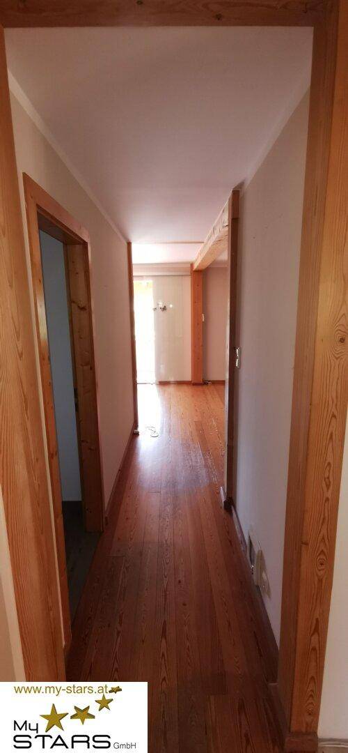 Langer Flur mit Holzdielenboden und hellen Wänden, der zu weiteren Räumen führt.