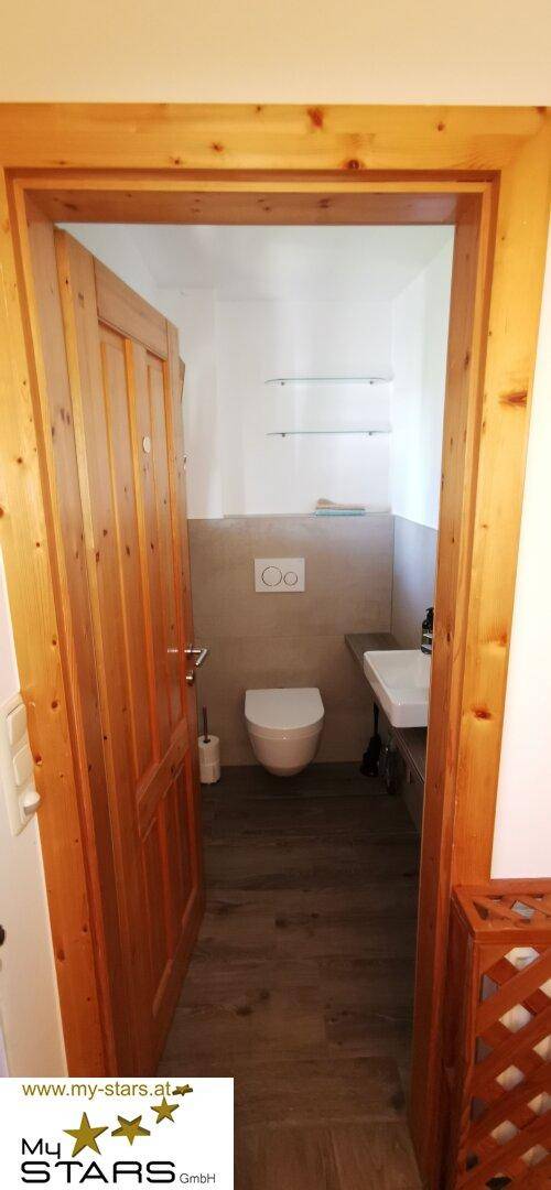 Modernes Gäste-WC mit wandhängendem WC, Waschbecken und Holzrahmen um die Tür.