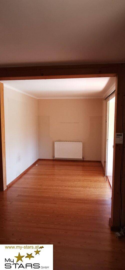 Geräumiges Wohnzimmer mit Holzdielenboden und einem Heizkörper unter dem Fenster.