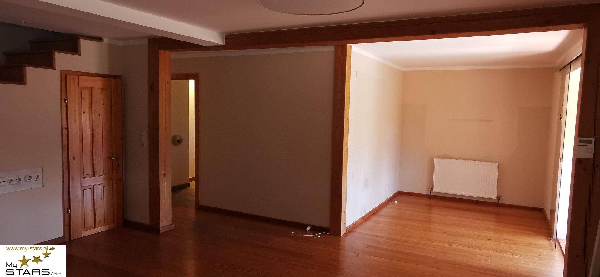 Heller Wohnbereich mit Holzdielenboden und breiten Türrahmen, der zu weiteren Räumen führt.