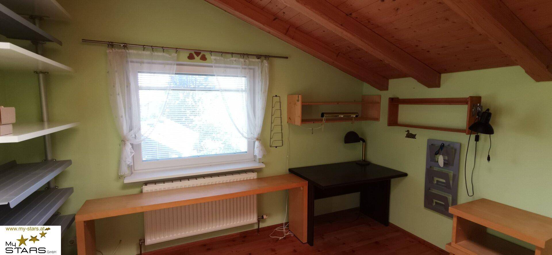 Helles Arbeitszimmer mit Holzbalkendecke, Fenster und einem Schreibtisch.