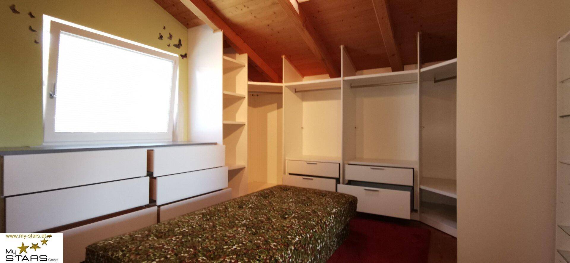 Begehbarer Kleiderschrank mit Regalen und Schubladen, unter einer Holzbalkendecke.