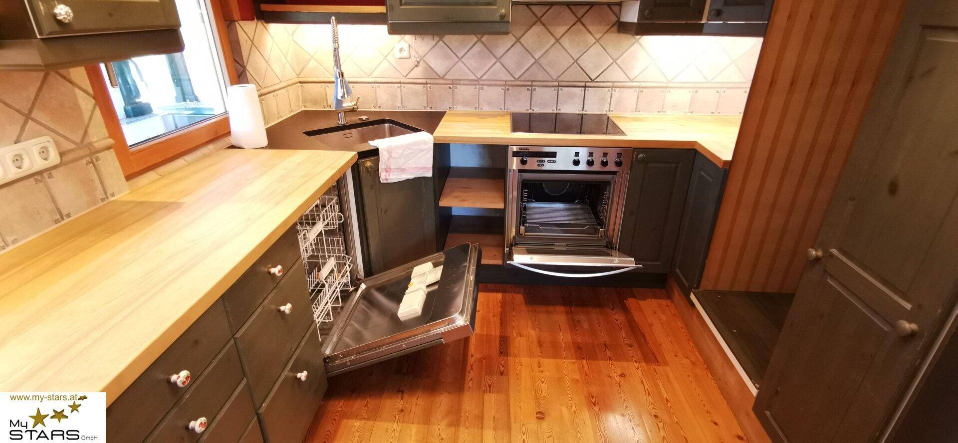 Funktionale Küche mit Holzarbeitsplatten, dunklen Schränken und eingebautem Geschirrspüler und Backofen.