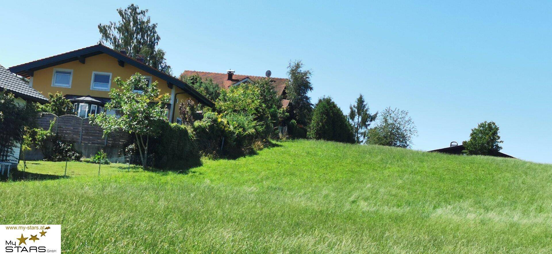 Haus auf einem grünen Hügel mit Bäumen unter blauem Himmel.