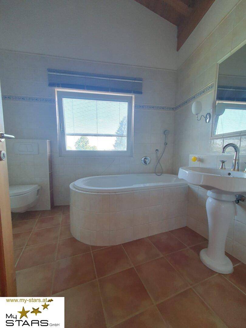 Helles Badezimmer mit Badewanne, Waschbecken, Toilette und Fenster für Tageslicht.