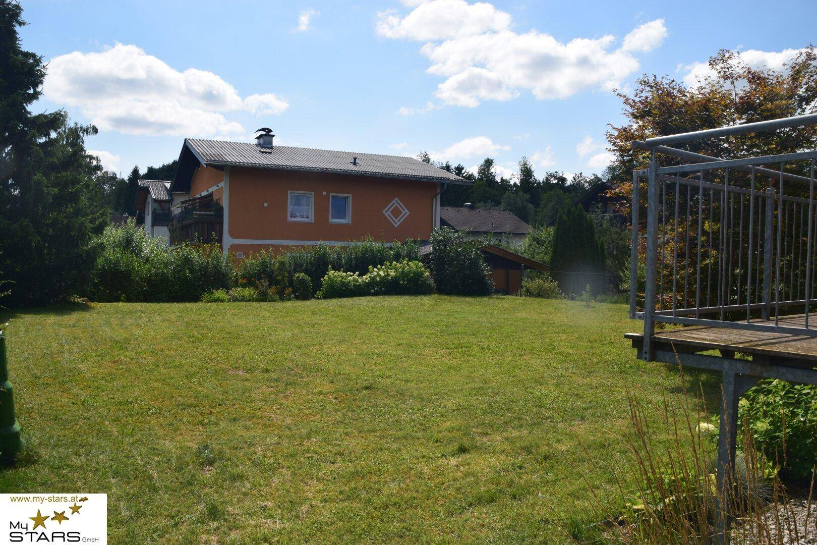 Rückansicht eines orangefarbenen Hauses mit Garten und Blick auf die umliegende Natur.