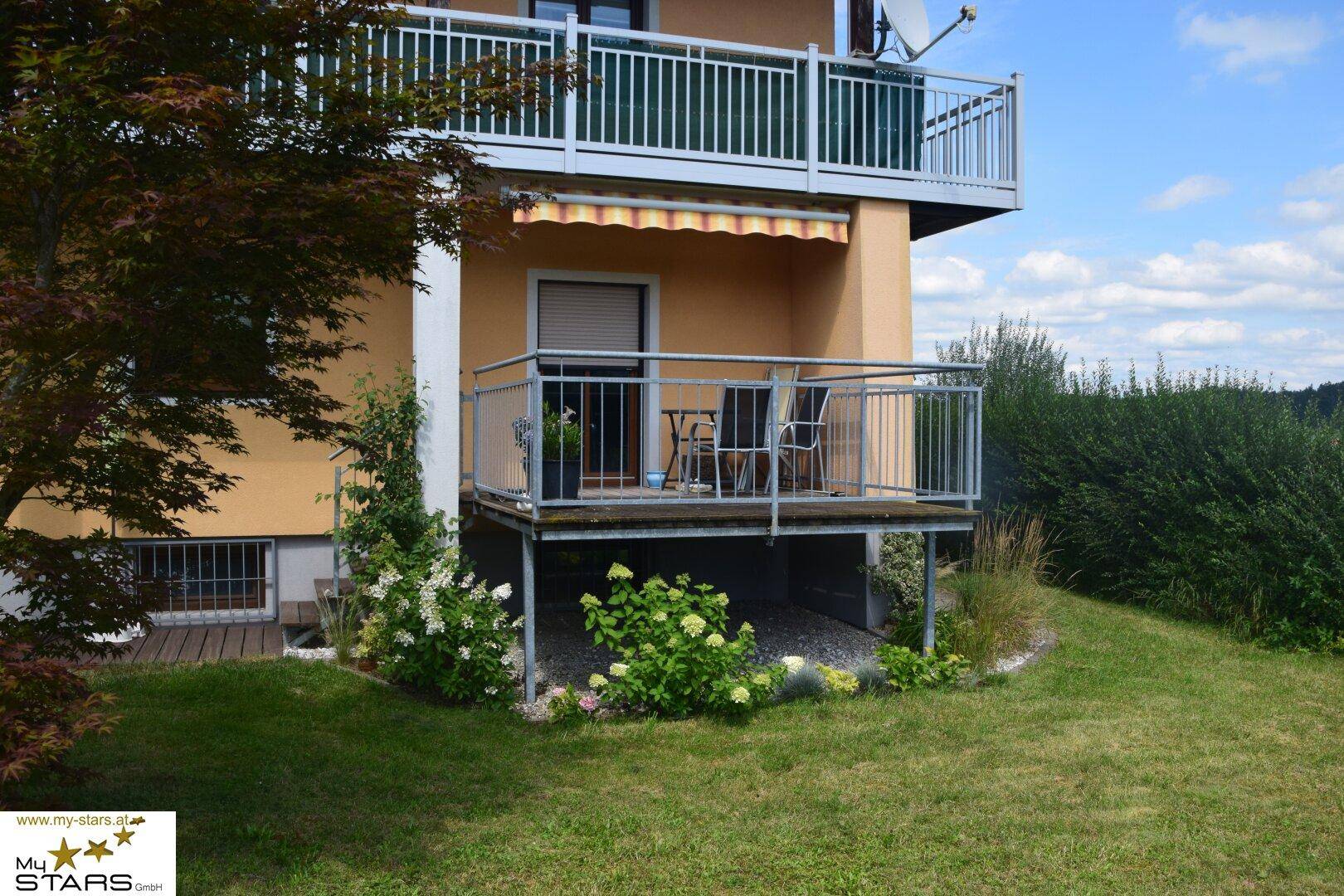 Gemütliche Terrasse mit Sitzgelegenheiten und Markise, umgeben von Blumen und Grün.