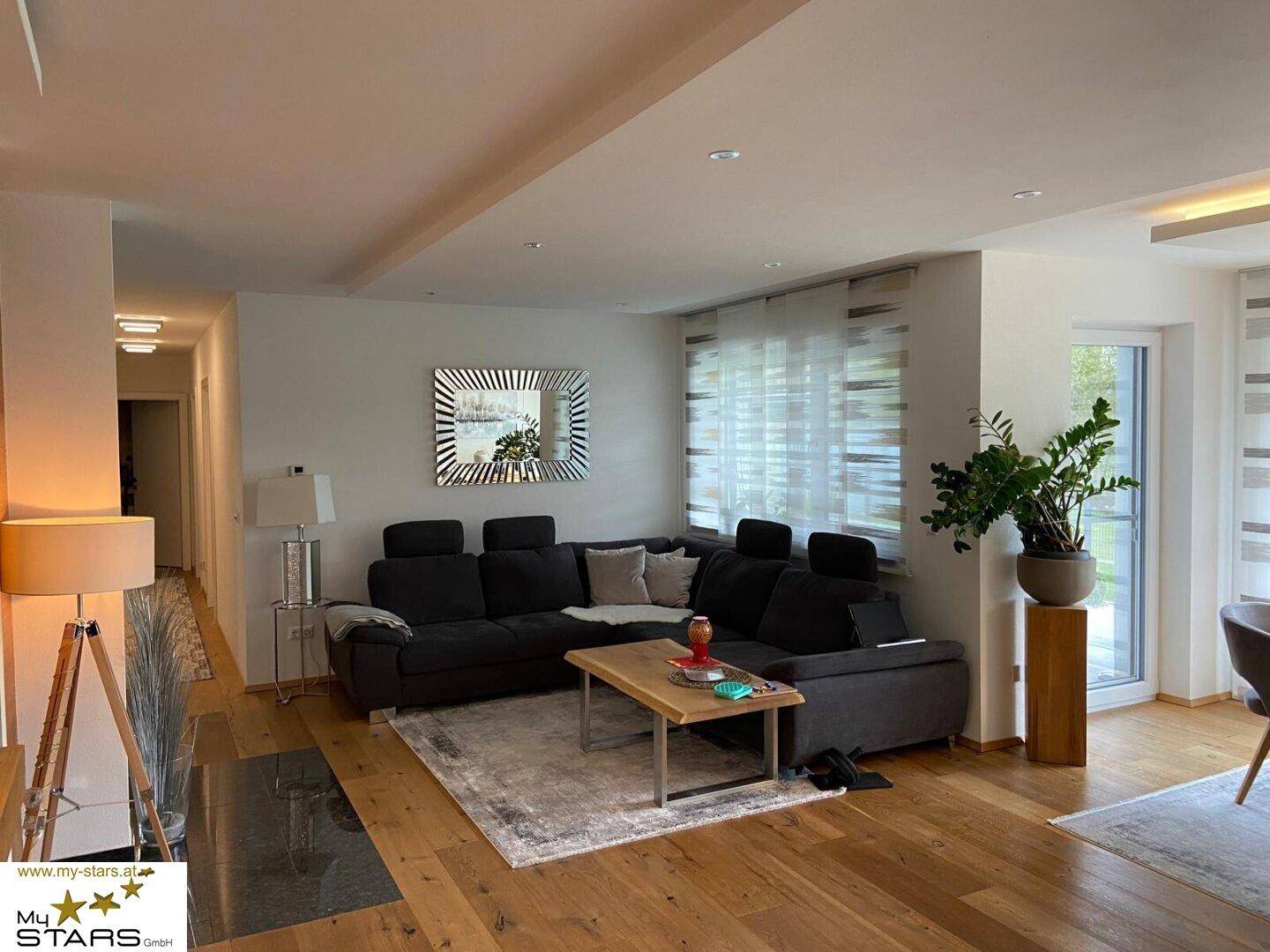Geräumiges Wohnzimmer mit großem Ecksofa, Holzboden und modernem Spiegel als Dekoration.